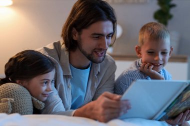 Baba yatağında çocuklarına masal okuyor.