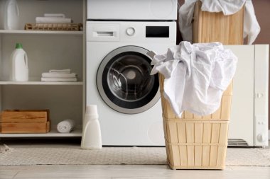 Çamaşır makinesi, raf ünitesi ve giysi dolu sepetli ev çamaşırhanesi.
