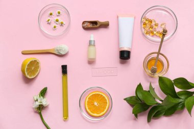 Doğal kozmetik ürünlerini pembe arka planda hazırlamak için numune ve malzemelerle dolu şişeler.