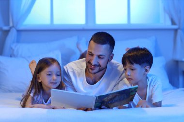 Mutlu baba ve çocuklar akşam evde masal okuyorlar.