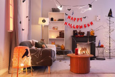 Gri kanepesi, şöminesi ve Cadılar Bayramı süslemeleri olan karanlık oturma odasının içinde.