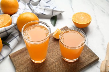 Tahta tahta tahta, lezzetli meyve suyu bardakları ve beyaz mermer arka planda taze portakallar.