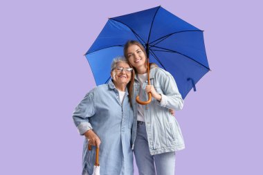 Mor arka planda şemsiyeleri olan mutlu yaşlı kadın ve torunu.