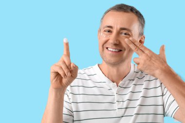 Mutlu olgun bir adam krem sürüyor ve mavi arka planda yüz geliştirme egzersizi yapıyor.