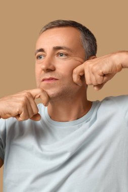 Olgun adam bej arka plan üzerinde yüz geliştirme egzersizi yapıyor.