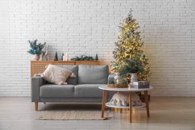 Oturma odasının içinde kanepe, masa ve parıldayan Noel ağacı var.