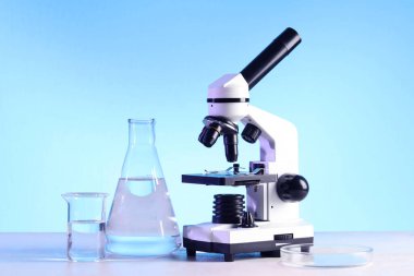 Modern mikroskop ve beyaz masanın üzerinde sıvı bulunan laboratuvar camları.