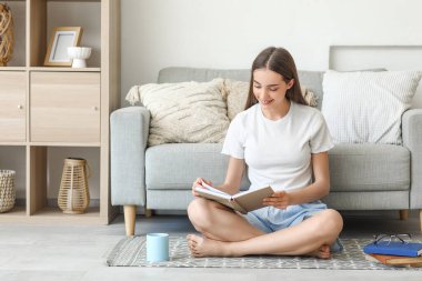 Evinde yerde çay fincanı okuyan güzel, genç ve mutlu bir kadın.