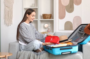 Evdeki kanepede bavulu ve ilk yardım çantasıyla mutlu genç bir kadın. Seyahat kavramı