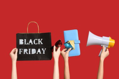 Alışveriş çantalı eller, megafon, kredi kartları ve kırmızı arka planda aksesuarlar. Kara Cuma indirimi