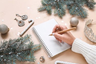 Not defterine bej arka planda Noel dekoru ve aksesuarları olan kadın, yakın plan