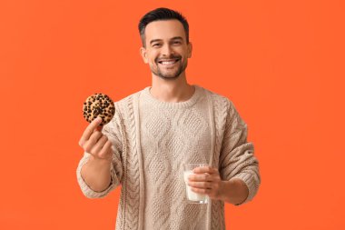 Lezzetli kurabiyesi ve turuncu arka planda bir bardak sütü olan yakışıklı adam.