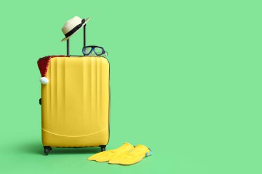 Plaj aksesuarları ve yeşil arka planda Noel Baba şapkası olan renkli bavul.