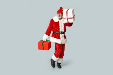 Gri arka planda hediye kutuları olan havalı Noel Baba.