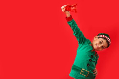 Kırmızı arka planda Noel hediyesi olan mutlu küçük elf.