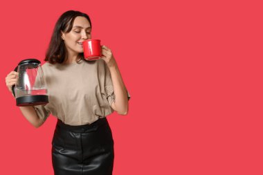 Modern elektrikli çaydanlığı olan genç ve güzel bir kadın kırmızı arka planda kahve içiyor.