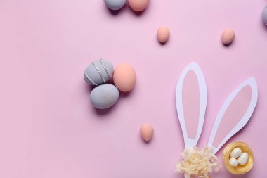 Boyanmış Paskalya yumurtaları, yuva ve mor arka planda kağıt tavşan kulakları olan kompozisyon