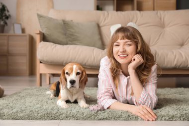 Evde halıya uzanmış sevimli av köpeği olan genç bir kadın.