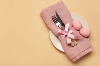 Paskalya yumurtaları, peçete ve bej arka planda çatal bıçak seti olan şık bir masa.