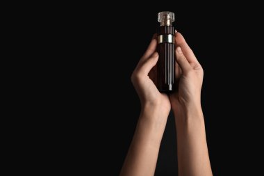 Siyah arka planda parfüm şişesi tutan kadın eller.