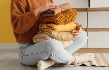 Temiz ve kalın giysileri olan bir kadın evinde yerde oturuyor.