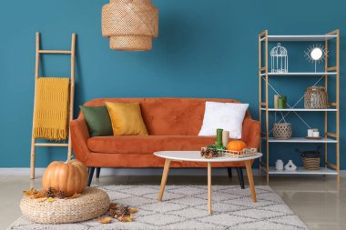 Oturma odasının içinde sonbahar dekoru olan rahat bir kanepe, puf ve kahve masası.