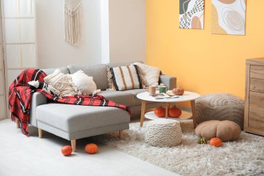 Gri koltuklu, kahve masalı, balkabaklı ve minderli bir sonbahar salonu.