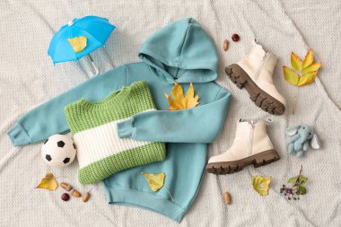 Hafif kumaş arka planında şık çocuk kıyafetleri, ayakkabıları, oyuncakları ve sonbahar yaprakları olan kompozisyon