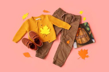 Pembe arka planda şık çocuk kıyafetleri, ayakkabıları, kitap ve kağıt sonbahar yaprakları olan kompozisyon
