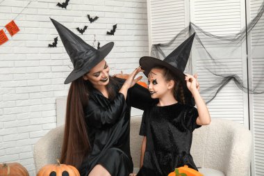 Cadılar Bayramı 'nı evde kutlayan küçük bir kız ve annesi cadı gibi giyinmiş.