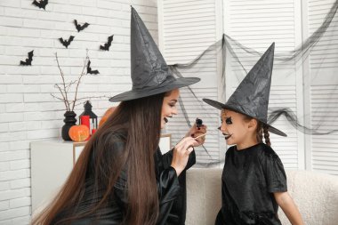 Anne Cadılar Bayramı için giyinmiş, evde kızının yüzünü boyuyor.