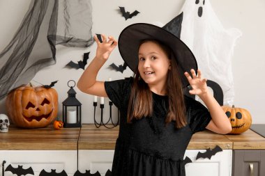 Cadılar Bayramı için dekore edilmiş balkabaklarıyla cadı gibi giyinmiş şirin küçük kız.