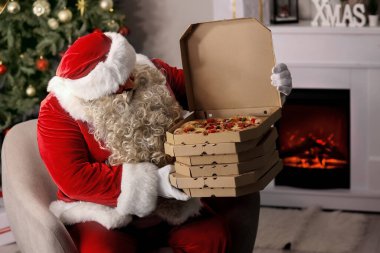 Noel Baba lezzetli pizzayla Noel arifesinde evdeki koltukta oturuyor.