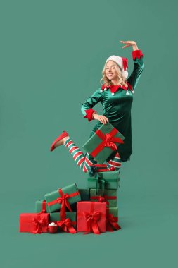 Yeşil arka planda Noel hediyeleri olan elf gibi giyinmiş güzel genç bir kadın.