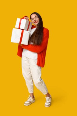 Sarı arka planda Noel hediyeleri taşıyan genç bir kadın.