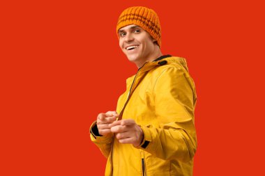 Kırmızı arka planda şık ceketli ve şapkalı genç bir adam.