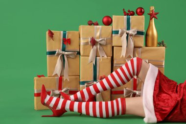 Noel çoraplı seksi kadın yeşil arka planda hediyelerin ve dekorasyonların yanında yatıyor.