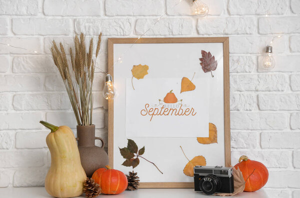 Тыквы, фото, камера и пшеница в вазе на каминной полке возле стены белого кирпича