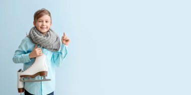 Açık mavi arkaplan üzerinde buz pateni tutan sevimli küçük çocuk.