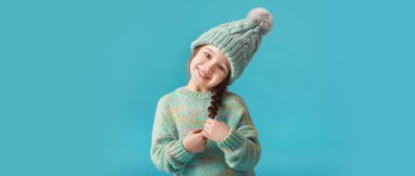 Açık mavi arka planda kışlık giysiler içinde şık küçük bir kız.