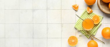 Beyaz fayanslı arkaplanda bir bardak lezzetli meyve suyu ve taze portakallar.