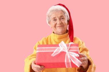 Noel Baba şapkalı yaşlı kadın pembe arka planda Noel hediyesi ile