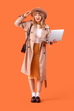 Sonbahar elbiseli, turuncu arka planda dizüstü bilgisayarı olan şık genç bir kadın.