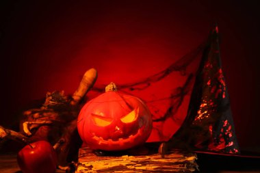 Cadılar Bayramı kompozisyonu, kriko-fener, eski kitap ve ağ ile ahşap masa karşı kırmızı arka plan, yakın çekim