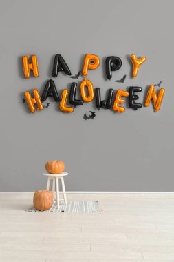 Tabure, balkabağı ve mesaj Odadaki gri duvarda asılı balonlardan yapılmış Mutlu Cadılar Bayramı