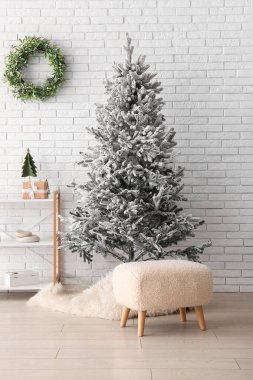 Beyaz tuğla duvarın yanında rafları ve minderleri olan güzel bir Noel ağacı