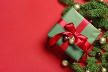 Noel ağacı dalları ve kırmızı arka planda topları olan bir hediye kutusu.