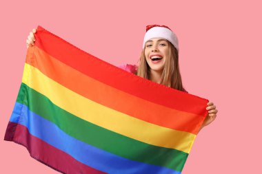 Pembe arka planda LGBT bayrağı olan Noel Baba şapkalı genç bir kadın.