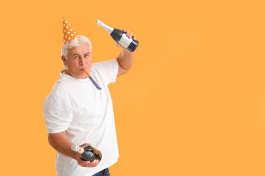 Parti şapkalı son sınıf öğrencisi elinde şampanya şişeleriyle Noel 'i turuncu arka planda kutluyor.