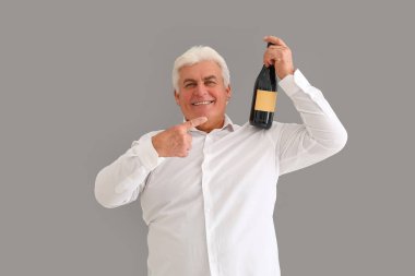 Gri arka planda bir şişe şampanyayla Noel 'i kutlayan mutlu kıdemli adam.